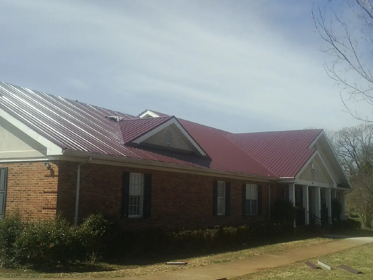 Red metal roof with gabled entries on a long brick building, from a Hail Damage Roof Repair job in Milford